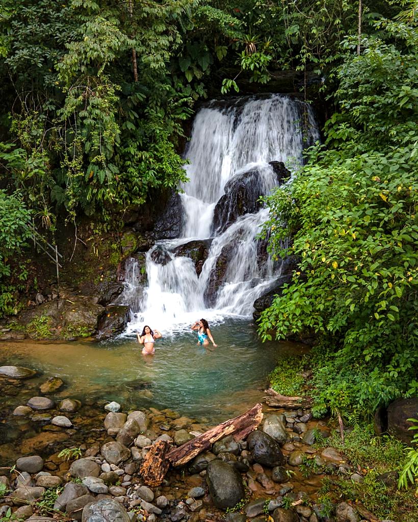 Two guests swimming in the pool below the waterfall