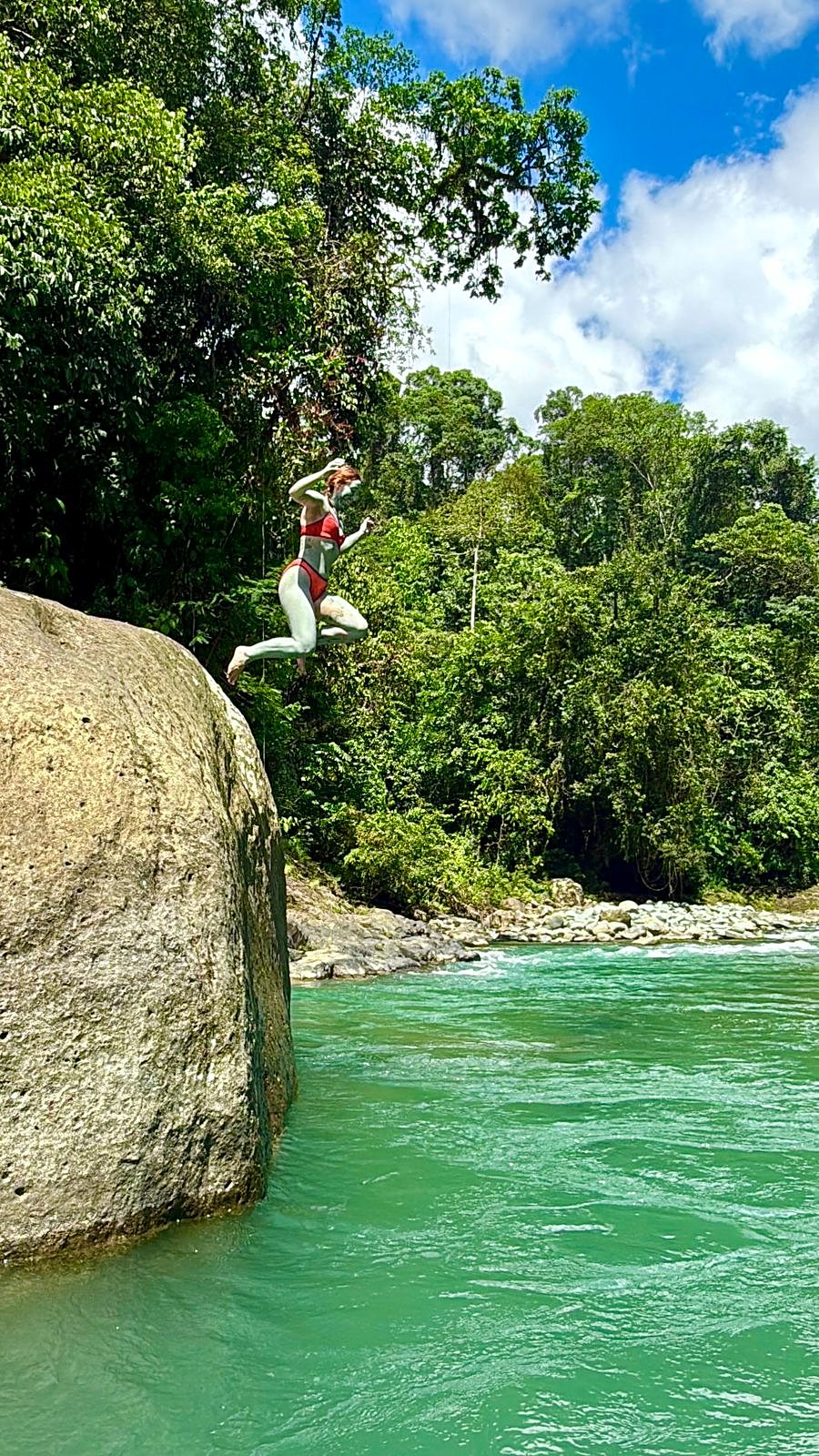 A guest jumping from a rock into the green river