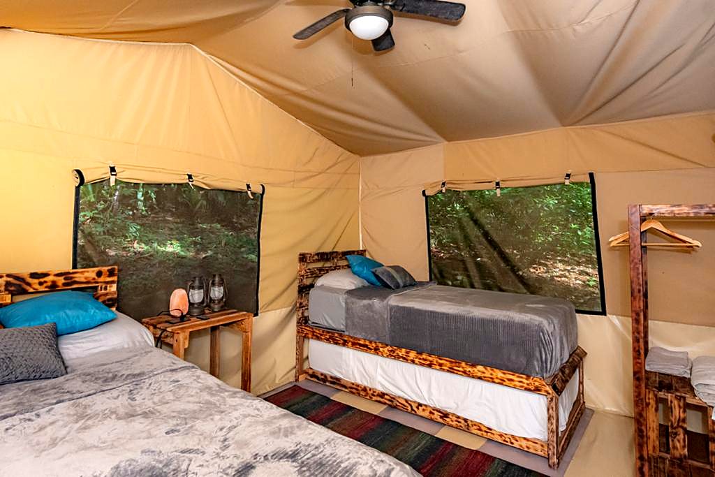 Inside a safari tent with two beds and a ceiling fan